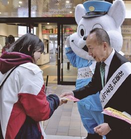 駅を利用する高校生（左）に啓発品を手渡す、田辺税務署の野間剛署長＝田辺市湊で