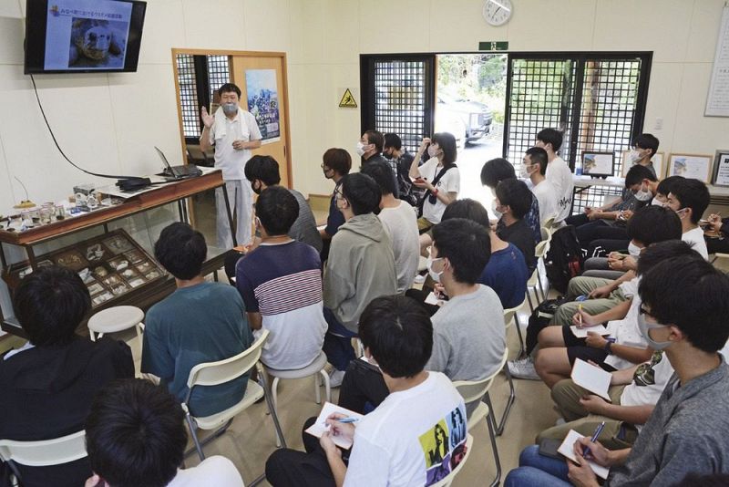 前田一樹副課長（左奥）からウミガメ保護活動の歴史についての話を聞く学生＝１２日、和歌山県みなべ町山内で