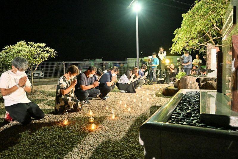 慰霊碑の前に犠牲になった人と同じ数の明かりを並べ、手を合わせる参列者（４日午前１時ごろ、和歌山県那智勝浦町で）