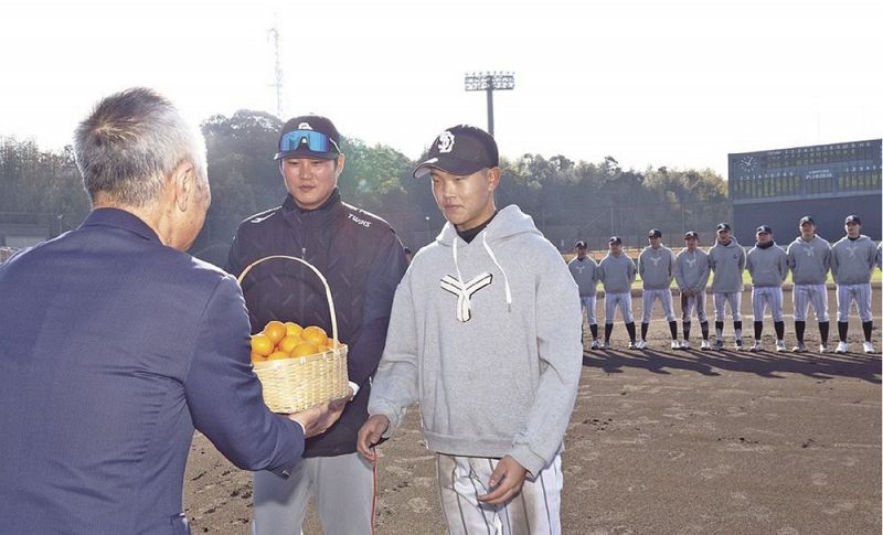 木村晃和副市長（左）から記念品のミカンを受け取る選手たち＝田辺市上の山１丁目で