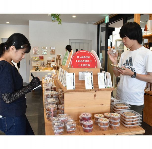 商品について説明を読んだりメモを取ったりする和歌山大学の学生（和歌山県田辺市湊で）